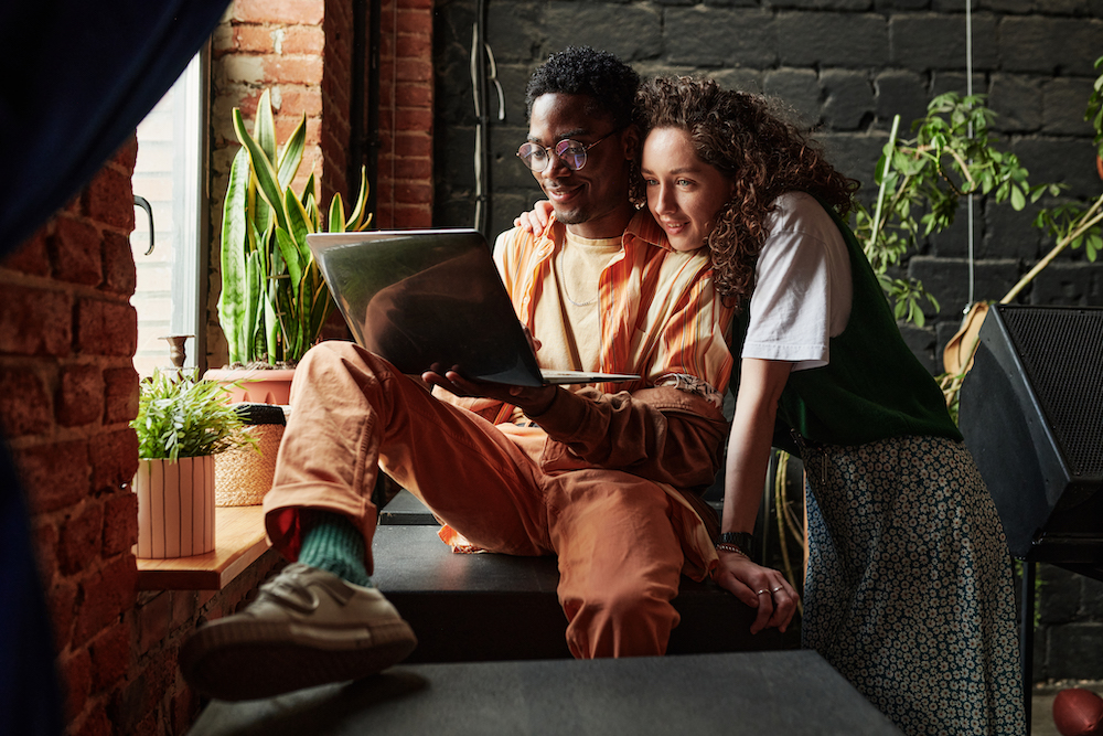 A happy young couple sits by the window with their laptop to plan their trip to Dead Cat Ranch.